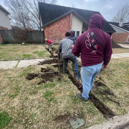 Yard Works men digging out drainage pipe under a sidewalk